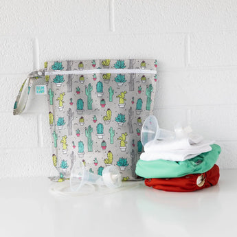 Bumkins Wet Bag: Cacti sits on a white table against a white brick wall with cloth diapers and breast pump parts in front.
