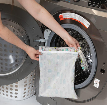 A person holds Bumkins Wet Bag: Cacti in front of an open front-loading washing machine.