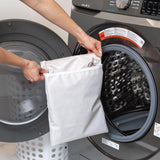 A person holds a Bumkins Wet Bag: Wander in front of an open front-loading washing machine.