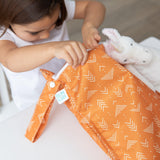A child opens a Bumkins Wet Bag: Grounded at a white table next to a stuffed unicorn.