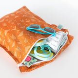 A partially open Bumkins Wet Bag: Grounded with sunglasses, a rolled-up cloth, and sandals on a white background.
