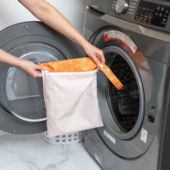 A person holds a Bumkins Wet Bag: Grounded in front of an open front-loading washing machine.