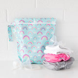 Bumkins Wet Bag: Rainbows sits on a white counter against a white brick wall with cloth diapers and breast pump parts in front.