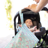 A person pushes a baby in a stroller with a Bumkins Wet Bag: Rainbows hanging from the handle.