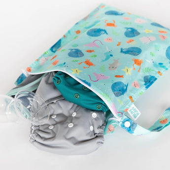 Bumkins Wet Bag: Ocean Life lays on a white background, with cloth diapers and breast pump parts peeking out.