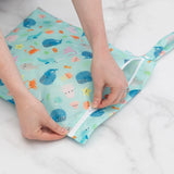 Hands zipping a Bumkins Wet Bag: Ocean Life on a marble surface.