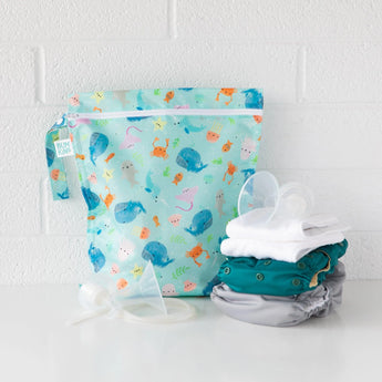 Bumkins Wet Bag: Ocean Life sits on a white table against a white brick wall, with cloth diapers and breast pump parts in front.