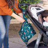 A woman unzips a Bumkins Wet Bag: Jungle to a stroller near some foliage as she strolls outside with her child.