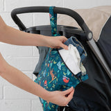 A person places clothes into a Bumkins Wet Bag: Jungle, made of waterproof fabric, attached to a stroller handle.