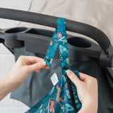 Close-up of hands attaching a Bumkins Wet Bag: Jungle to a stroller handle using the snap button on the strap.