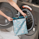 A person holds Bumkins Wet Bag: Jungle in front of a front-loading washing machine.