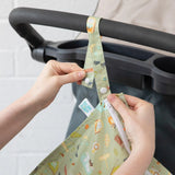 Hands attach a Bumkins Wet Bag: Camp Gear to a stroller handle using the snap button closure on the strap.