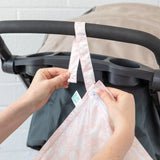 Hands attach a Bumkins Wet Bag: Lace to a stroller handle using the snap button on the strap.