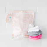 Bumkins Wet Bag: Lace sits on a white table against a white brick wall, with cloth diapers and breast pump parts in front.