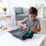 A child in a gray shirt opens a Bumkins Wet Bag: Mickey Mouse Icon Black + White at a white table in a living room with toys and flowers.