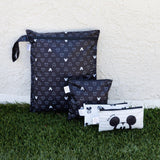 Bumkins Wet Bag: Mickey Mouse Icon Black + White sits on grass against a beige textured wall with three other bags.
