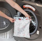 A person holds Bumkins Wet Bag: Mickey Mouse Classic in front of an open front-loading washing machine.