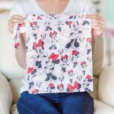 A person sitting on a beige couch holds a Bumkins Wet Bag: Minnie Mouse Classic.