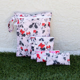 Bumkins Wet Bag: Minnie Mouse Classic sits by smaller, similarly printed pouches on grass against a beige textured wall.