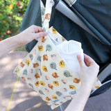 Close-up of hands placing a cloth into a Bumkins Wet Bag: Winnie and Friends hanging from a stroller handle outdoors