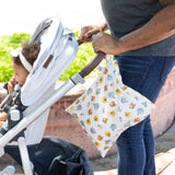 An adult pushes a stroller with a child outdoors, as a Bumkins Wet Bag: Winnie and Friends hangs from the handle.