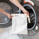 A person holds Bumkins Wet Bag: Winnie and Friends in front of a front-loading washing machine.