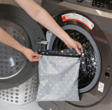 A person holds Bumkins Wet Bag: Super Mario™ Lineup in front of an open front-loading washing machine.