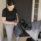 A woman in green top and gray pants zips a Bumkins Wet Bag: Super Mario™ Lineup attached to a stroller in front of a door.