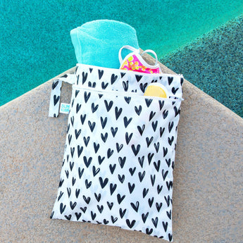 Bumkins Wet/Dry Bag: Hearts sits near a pool, filled with a towel, swimsuit, and sunscreen.