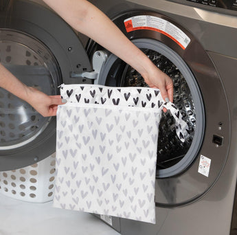 A person holds Bumkins Wet/Dry Bag: Hearts in front of an open front-loading washing machine.