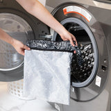 A person holds a Bumkins Wet/Dry Bag: Be Kind in front of an open front-loading washing machine.