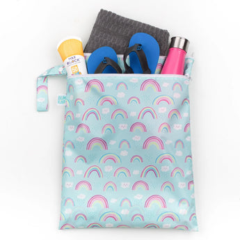 Bumkins Wet/Dry Bag: Rainbows holds flip-flops, a towel, sunscreen, and a pink water bottle on a white background.