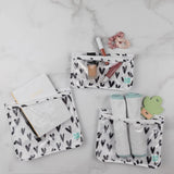 Bumkins Clear Travel Bag 3-Pack: Hearts holds a notebook, makeup, burp cloths, and a teether on a marble background.
