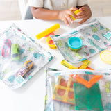 A child plays with toys and play dough at a white table with Bumkins Clear Travel Bag 3-Pack: Cacti nearby.