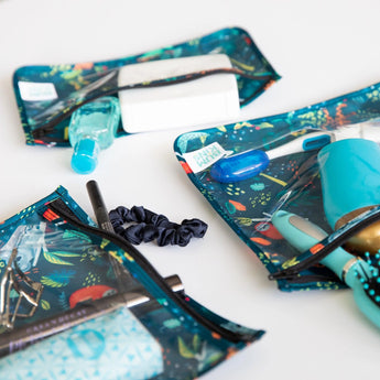 Close-up of Bumkins Clear Travel Bag 3-Pack: Jungle with toiletries and makeup on a white background.