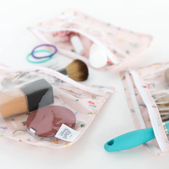 Close-up of Bumkins Clear Travel Bag 3 Pack: Princess Magic with makeup and brushes on a white background.