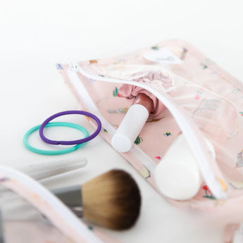 Close-up of Bumkins Clear Travel Bag 3 Pack: Princess Magic with brushes, hair ties, and lipstick on a white background.