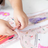 Close-up of a child zipping a Bumkins Clear Travel Bag 3 Pack: Princess Magic with a notebook; another bag with markers sits nearby.