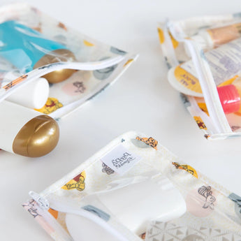Close-up of Bumkins Clear Travel Bag 3-Pack: Winnie and Friends filled with toiletries on a white background.
