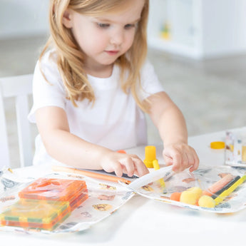 A child explores toys and art supplies in Bumkins Clear Travel Bag 3-Pack: Winnie and Friends at a white table.