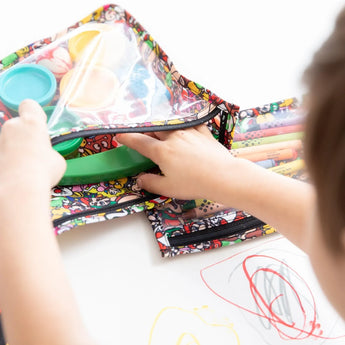 Close-up of a child sorting art supplies in Bumkins Clear Travel Bag 3-Pack: Super Mario™ Mashup, with crayons and drawings on the table.