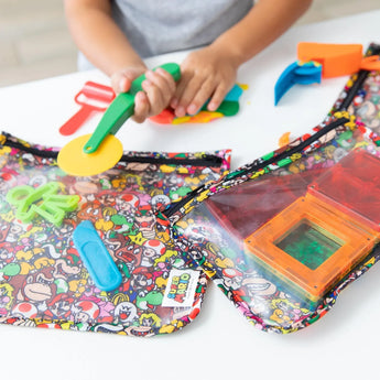 Close-up of child playing with colorful clay and tools next to Bumkins Clear Travel Bag 3-Pack: Super Mario™ Mashup with magnetic blocks.