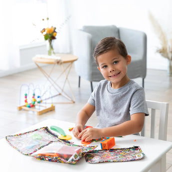 A child plays with colorful toys at a table with Bumkins Clear Travel Bag 3-Pack: Super Mario™ Mashup in a bright living room.