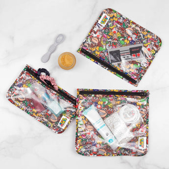Bumkins Clear Travel Bag 3-Pack: Super Mario™ Mashup holds baby items and toiletries, with a spoon and food jar on a marble background.