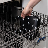 A person places Bumkins Silicone Bib: Mickey Mouse Faces in the top rack of an open dishwasher.