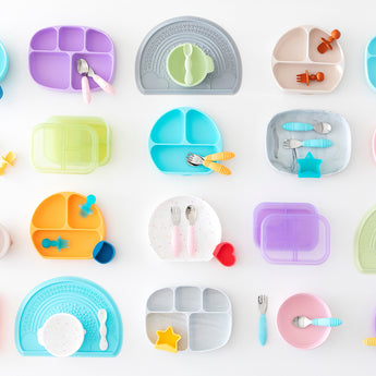 A flat lay of colorful childrens plates, utensils, and cups arranged in a grid pattern on a white surface. Each set is neatly organized and varies in shape and color.