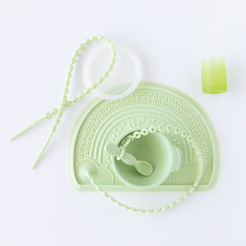 A set of light green silicone baby feeding items, including a bib, bowl, spoon, cup, beaded teether, and a textured zip tie, all arranged neatly on a white background.