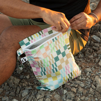A man sits on the ground while opening a Roamio by Bumkins Motley Check Wet Bag.