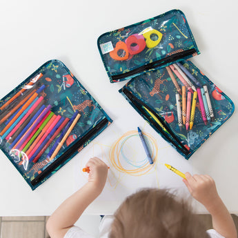 Children's art supplies including markers and colored pencils in Bumkins Jungle Animals Clear Travel Bags on a table. A child is drawing on the paper surface.