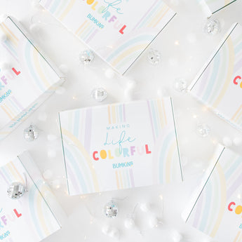 Several pastel-colored boxes with the words Making Life Colorful BUMKINS are arranged on a white surface, surrounded by small white balls and silver disco balls.